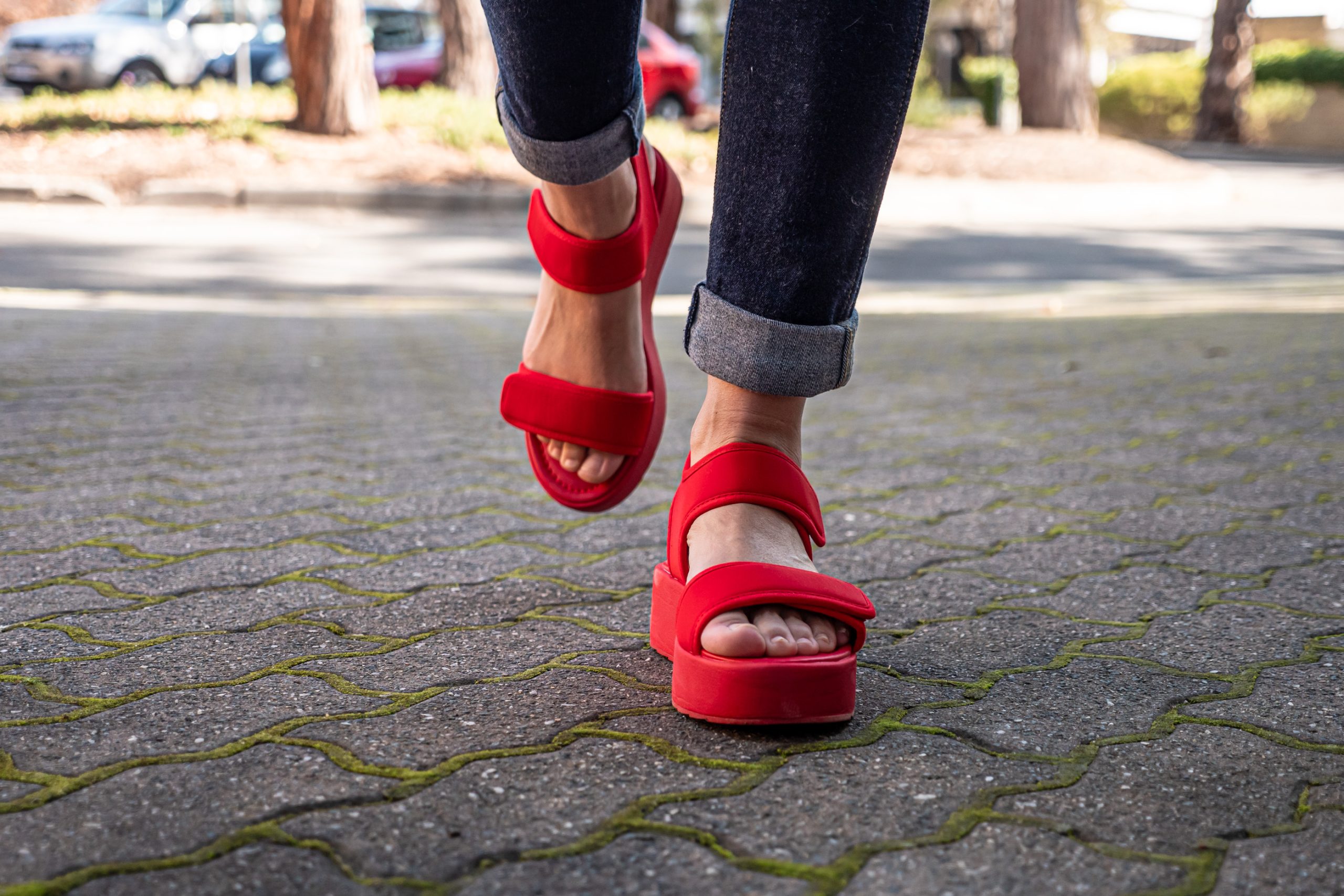 Close up of a person's feet while walking and wearing red sandals.