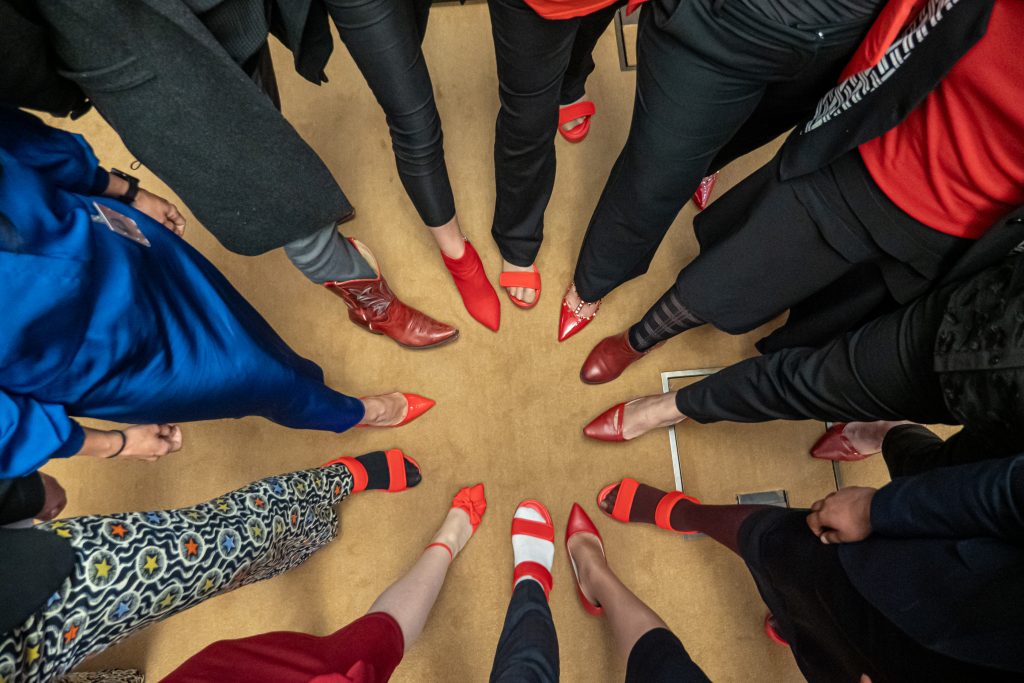 People's feet forming a circle, all wearing red shoes.
