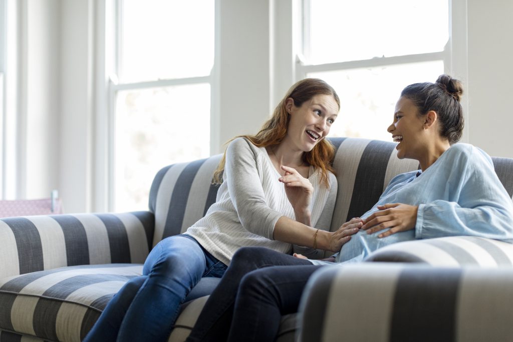 A pregnant woman and her friend talking together while sitting on a couch